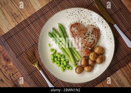 Steak de thon grillé servi avec asperges, pommes de terre rôties, haricots édamames et sauce hollandaise sur une assiette, vue du dessus Banque D'Images