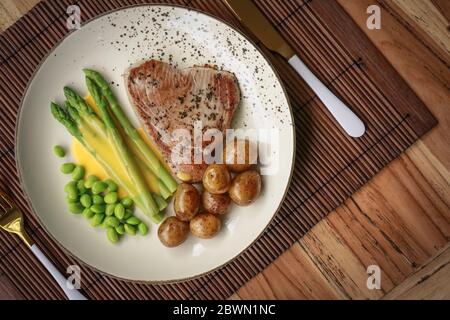 Steak de thon grillé servi avec asperges, pommes de terre rôties, haricots édamames et sauce hollandaise sur une assiette, vue du dessus Banque D'Images