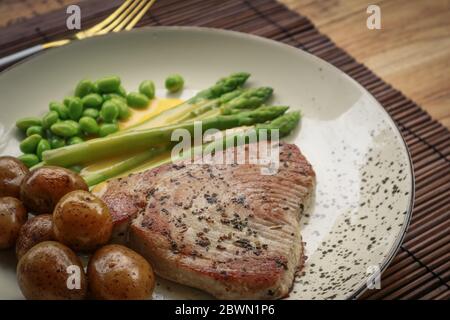 Steak de thon grillé servi avec asperges, pommes de terre rôties, haricots édamames et sauce hollandaise sur une assiette, vue du dessus Banque D'Images