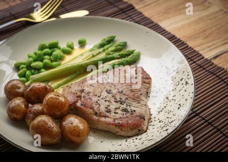 Steak de thon grillé servi avec asperges, pommes de terre rôties, haricots édamames et sauce hollandaise sur une assiette, vue du dessus Banque D'Images