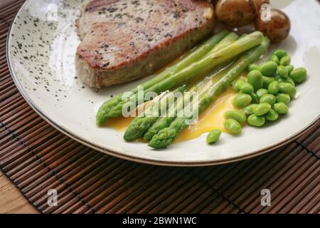 Steak de thon grillé servi avec asperges, pommes de terre rôties, haricots édamames et sauce hollandaise sur une assiette, vue du dessus Banque D'Images