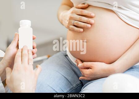 Médecin tenant quelques médicaments ou suppléments pour une femme enceinte pendant une consultation, vue rapprochée centrée sur le ventre enceinte. Concept de médicament pour les femmes enceintes Banque D'Images