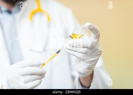 Médecin en prenant un vaccin ou un médicament dans une seringue, vue rapprochée centrée sur les mains sur le fond jaune Banque D'Images