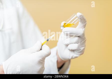 Médecin en prenant un vaccin ou un médicament dans une seringue, vue rapprochée centrée sur les mains sur le fond jaune Banque D'Images