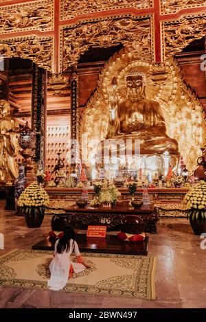 Fille bouddhiste priant devant un Bouddha doré Temple de bái ÄÃ­nh Banque D'Images