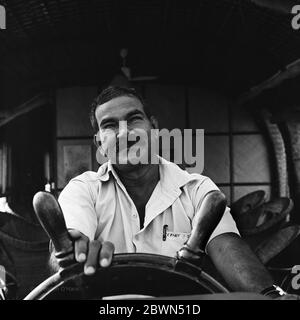 Souriant, moustachié, skipper à la doe-eyed casualy fait tourner la roue du bateau pour garder le Kettuvallam sur le parcours dans les eaux du Kerala. Banque D'Images