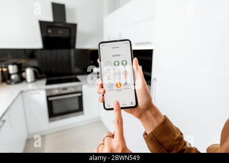 Femme contrôlant des appareils de cuisine avec un smartphone, gros plan sur un appareil mobile avec application Smart Home lancée. Concept de maison intelligente Banque D'Images