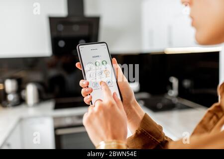 Femme contrôlant des appareils de cuisine avec un smartphone, gros plan sur un appareil mobile avec application Smart Home lancée. Concept de maison intelligente Banque D'Images