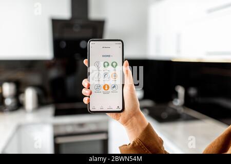 Femme contrôlant des appareils de cuisine avec un smartphone, gros plan sur un appareil mobile avec application Smart Home lancée. Concept de maison intelligente Banque D'Images