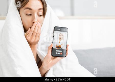 Portrait d'une femme couverte d'une couverture blanche appelant un médecin avec un smartphone, se sentant mal à la maison. Concept de médecine en ligne Banque D'Images