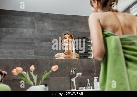 Jeune et belle femme prenant soin d'elle-même, regardant dans le grand miroir à la salle de bains à la maison Banque D'Images