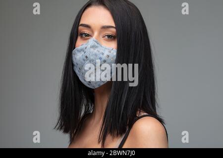 Jeune femme dans un masque en tissu à la mode en tissu à motifs tournant pour regarder la caméra sur un fond gris conceptuel de post Covid-19 li Banque D'Images