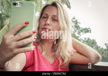 Femme blonde adulte tenant et utilisant un smartphone pour selfie en plein air sur l'île de Bali, Indonésie. Banque D'Images