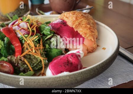 Saumon fumé, pommes de terre sautées, tomates cerises semi-séchées, sauce aux betteraves, œufs pochés, croissant au beurre chaud, ciboulette, herbes mélangées, pistaches Banque D'Images