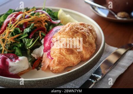 Saumon fumé, pommes de terre sautées, tomates cerises semi-séchées, sauce aux betteraves, œufs pochés, croissant au beurre chaud, ciboulette, herbes mélangées, pistaches Banque D'Images