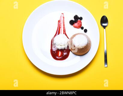 Fondant au chocolat blanc avec glace à la vanille et sauce aux fraises sur fond jaune. Concept de confiserie. Gâteau de lave fondu et baies sur l'assiette. Dessert servi dans un café, un restaurant ou une boulangerie Banque D'Images