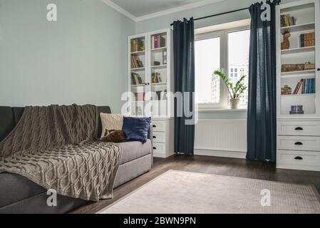 Chambre pour adolescents lumineuse et confortable avec bibliothèques blanches, canapé gris et murs bleus Banque D'Images