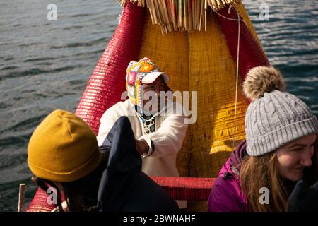 L'homme de la communauté Uros sur le bateau traditionnel fait de totora roseaux avec les touristes, portant un bonnet traditionnel Banque D'Images