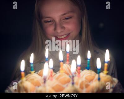 Une jeune fille admire des bougies allumées au gâteau à son anniversaire. Banque D'Images