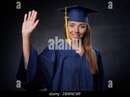 Jeune femme souriante agitant la main portant une casquette et une robe bleues Banque D'Images
