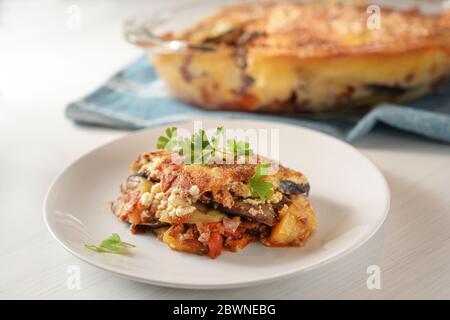 Moussaka, casserole traditionnelle grecque cuite d'aubergines, pommes de terre, viande hachée et tomates servies avec garniture de persil sur une assiette sur une table blanche, Banque D'Images