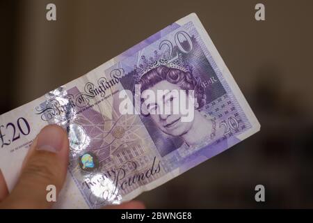 Personnes donnant la main de la monnaie de l'Angleterre au Royaume-Uni - un violet vingt livre note s'étaler sur un fond marron. Change. Banque D'Images