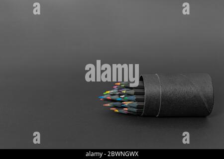 Boîte porte-crayons noire pleine de crayons de couleur sur fond sombre. Crayons de différentes couleurs Banque D'Images