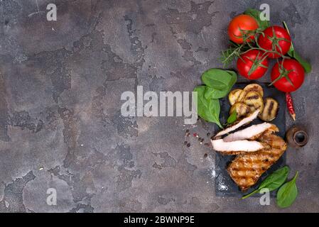 Coupe de pins et des steaks grill poulet, les tomates, le maïs et les pommes de terre sur une grille avec le basilic et le romarin sur un fond en béton noir Banque D'Images