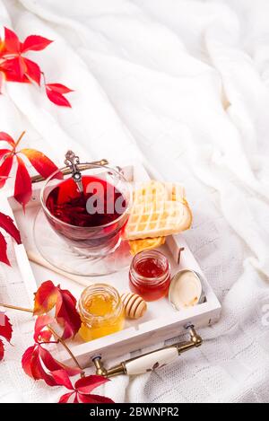 Petit déjeuner avec thé rouge, miel et gaufres sur un lit, plats faits maison en automne Banque D'Images