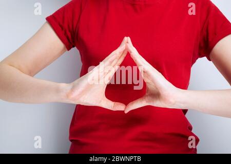 Une jeune fille en T-shirt rouge montre ses mains sur fond gris. Symbole de don de sang Banque D'Images