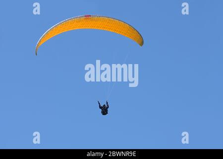 Le pilote de parapente avec un planeur jaune orange vole dans le ciel bleu clair, sport d'aventure de loisir et de compétition, grand espace de copie Banque D'Images