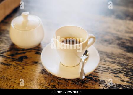 Café frais aromatique dans une tasse blanche. Americano avec un bol à sucre sur la table dans le café. Americano dans une petite tasse blanche Banque D'Images