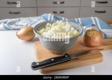 Oignons entiers et hachés dans un bol, un couteau et une planche à découper sur une table blanche dans la cuisine, point choisi Banque D'Images