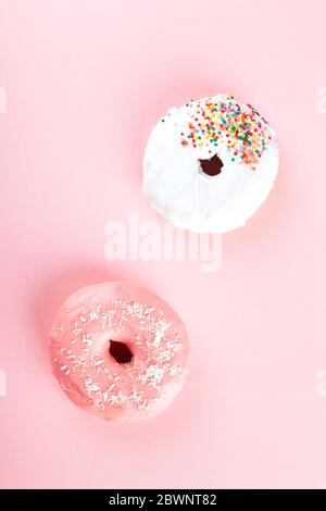 Beignet avec glaçage blanc et rose et garniture de pâtisserie au sucre multicolore sur fond rose. Vue de dessus Banque D'Images
