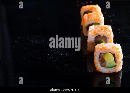 California Maki Sushi avec Masago - rouleau de viande de crabe, avocat, concombre sur fond noir de verre, espace de copie Banque D'Images