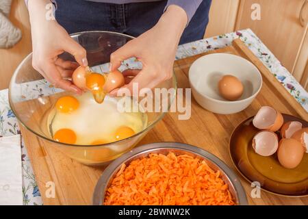 Les mains des femmes cassent l'œuf et séparent le jaune en protéine. Préparation du gâteau de carottes. Un bol en métal rempli de carottes râpées est sur le compte Banque D'Images