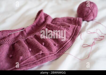 Une jupe tricotée rose se trouve sur le lit, un fond blanc d'une feuille blanche, des fils de laine et une pelote de fil se trouvent à proximité Banque D'Images