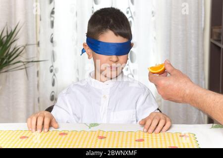 Un petit garçon de 8 ans qui a les yeux bandés et qui goûtant un morceau d'orange. Banque D'Images