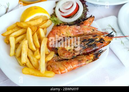 Gros plan sur les crevettes grillées de grande taille avec des pommes de terre frites, des légumes et du citron, déjeuner au restaurant. Banque D'Images