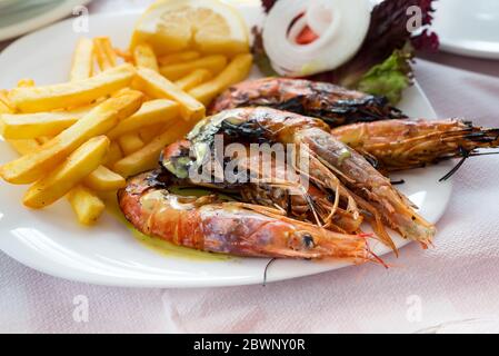 Gros plan sur les crevettes grillées de grande taille avec des pommes de terre frites, des légumes et du citron, déjeuner au restaurant. Banque D'Images