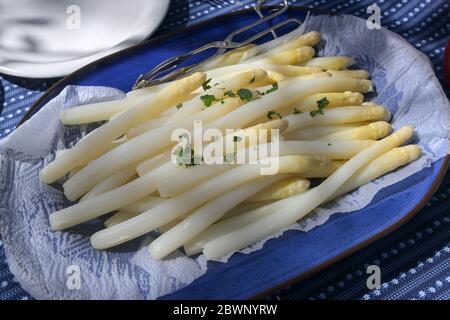 Asperges blanches cuites servies avec garniture aux herbes sur une assiette bleue sur la table, concentration sélectionnée, profondeur de champ étroite Banque D'Images