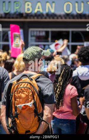 05-30-2020 Tulsa USA - Homme en casquette avec sac à dos orange et masque Covid se dresse à l'arrière de la foule de manifestants avec Urban Outfitters en arrière-plan Banque D'Images
