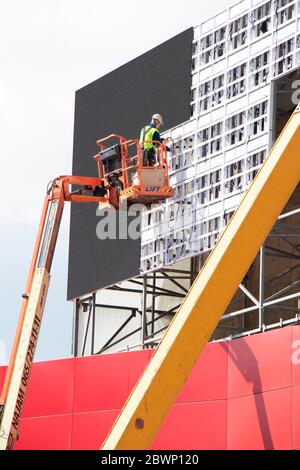 Belgrade, Serbie - 6 mai 2020: Ouvrier de construction dans un panier de grue installant des feuilles de revêtement pour couvrir la structure métallique sur un mur de façade de bâtiment Banque D'Images