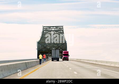 deux hommes de race blanche marchant le long du côté de l'autoroute sous un pont en béton de grande hauteur avec des semi-camions roulant à grande vitesse. Banque D'Images