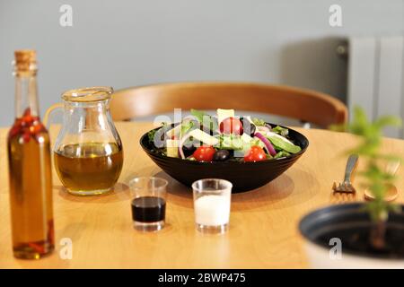 Salade méditerranéenne avec pot d'huile d'olive, bouteille d'huile d'olive avec piment rouge à l'intérieur de la bouteille, vinaigre noir, sel. Photo vue de face Banque D'Images