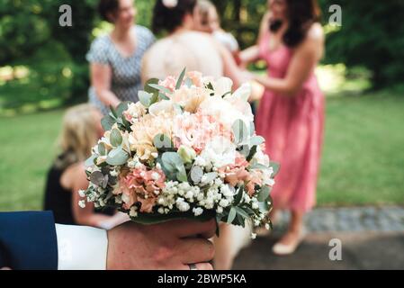 Homme main tenant coloré joli bouquet de mariage. Flou jeune femmes attirantes à la fête de mariage en arrière-plan. Banque D'Images
