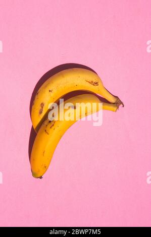 Photo fermée de deux bananes jaunes avec taches sombres sur une surface rose avec forte lumière du soleil Banque D'Images