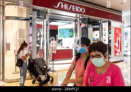 Les clients portant des masques faciaux se promène devant la société multinationale japonaise de soins personnels Shiseido, dans le centre commercial de Hong Kong. Banque D'Images