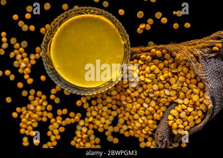 Pâte de pois chiches fraîchement bouillie dans un bol en verre sur la surface noire avec quelques lentilles de pois chiches crues. Banque D'Images