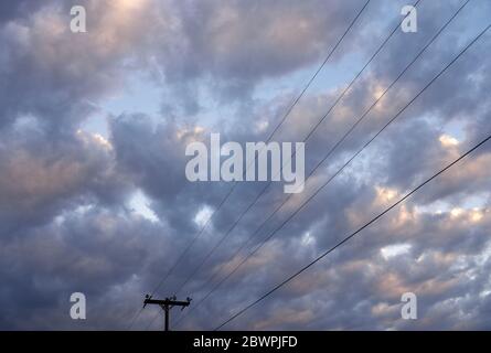 Poteaux de service et lignes d'alimentation aériennes contre le ciel et les nuages au coucher du soleil dans le Wyoming, États-Unis Banque D'Images